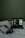 A dimly lit scene featuring a laptop placed on a white bedspread. The laptop screen displays a music streaming interface with album art and track information. Next to the laptop, there is a camera with a strap lying on the bed.
