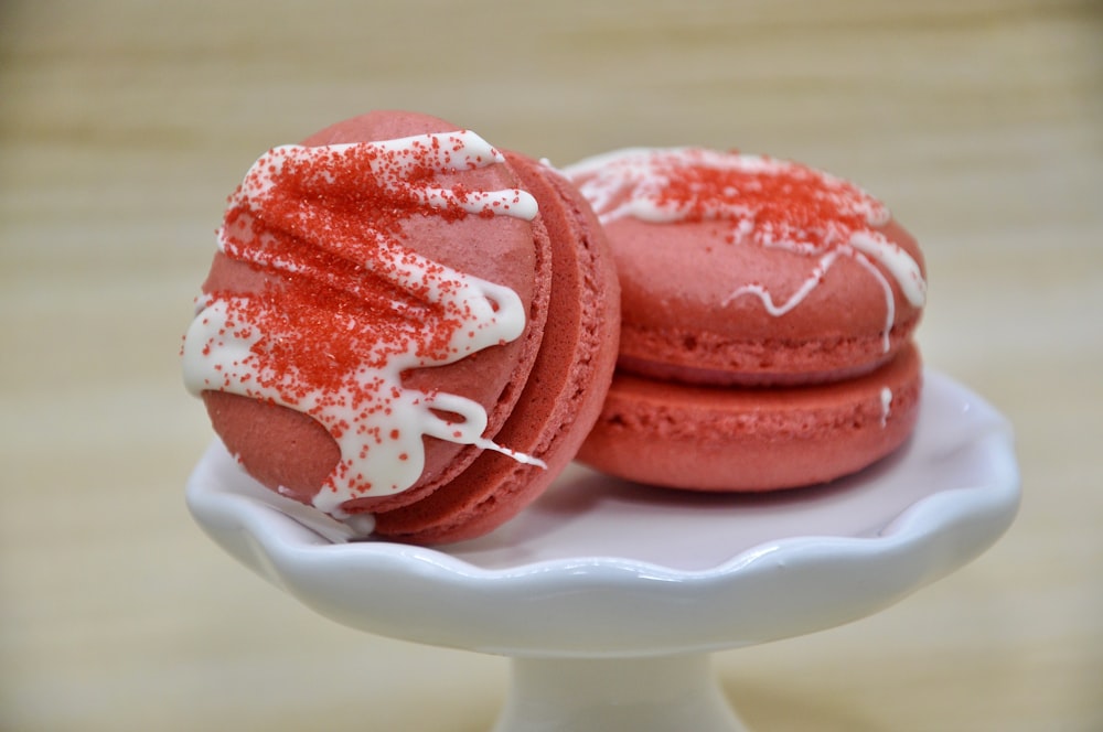 two red macaroons with white icing on a white plate