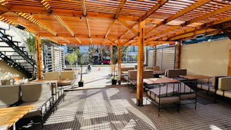 a patio with tables and chairs under a wooden roof