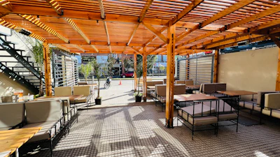 a patio with tables and chairs under a wooden roof