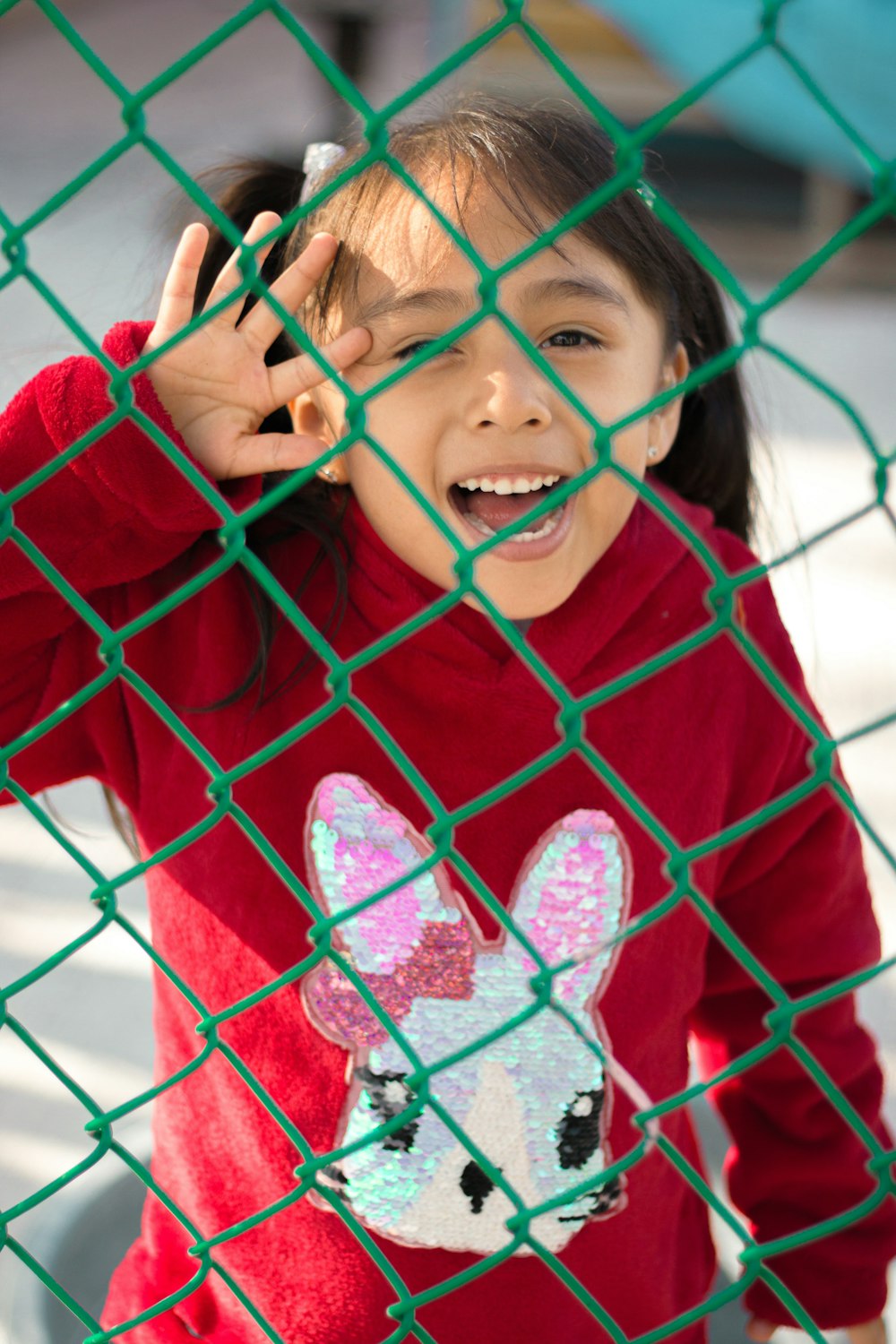 a little girl standing behind a green fence