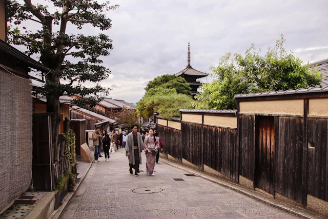 Visitors in kimono walk the cobblestone lane of Ninenzaka with the Yasaka Pagoda rising behind the rooftops.