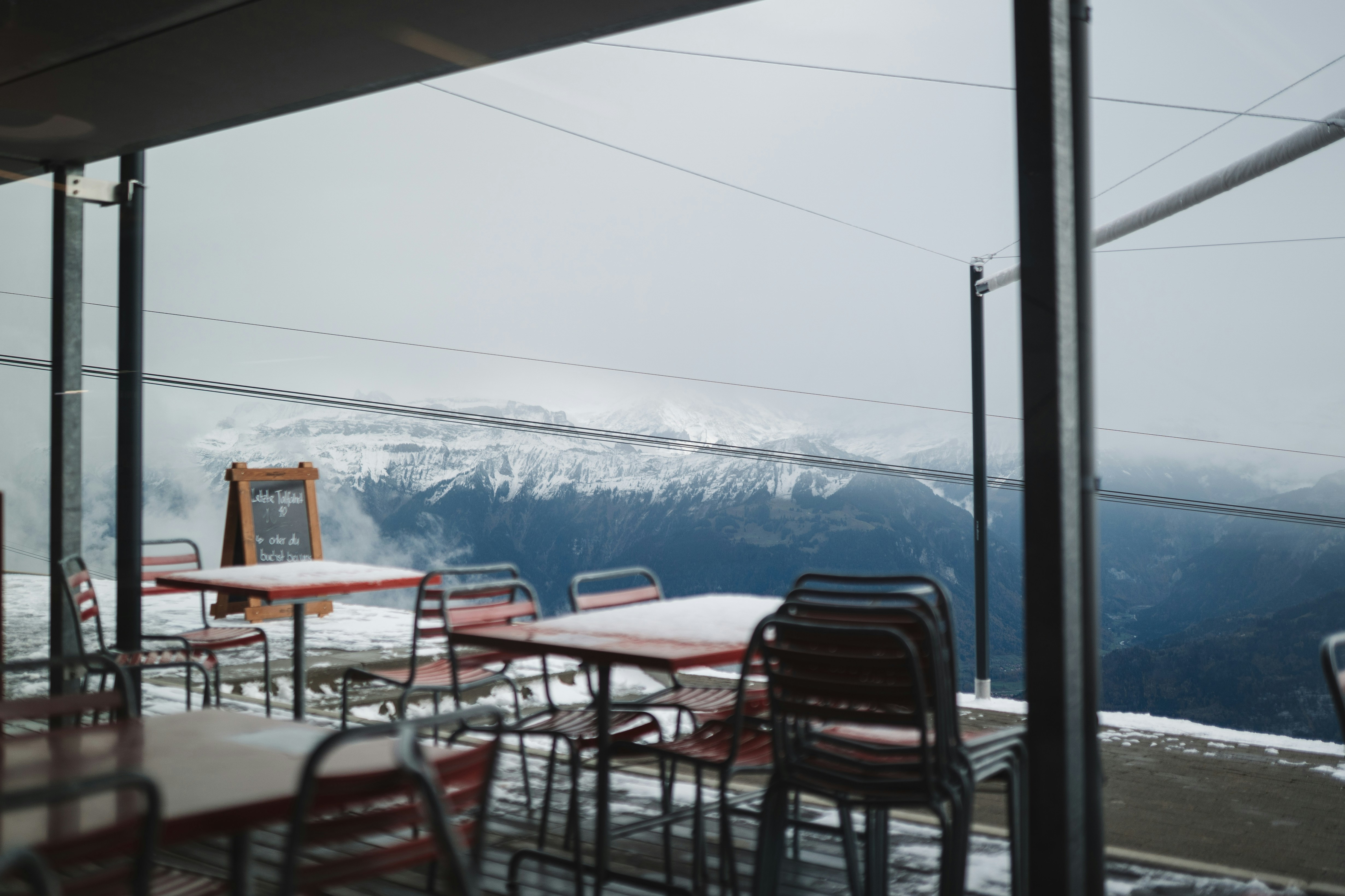 A sunny mountain-restaurant terrace with a table set out facing the snow-capped Alps