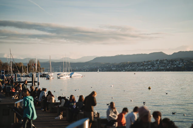 A cozy gathering of neighbors chatting happily by the lake under soft evening light.