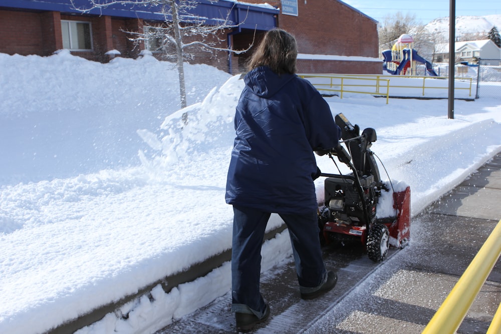 a woman using a snow blower to clear snow from the sidewalk