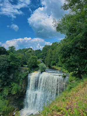 A vibrant waterfall tumbling over mossy green rocks under a bright blue sky.