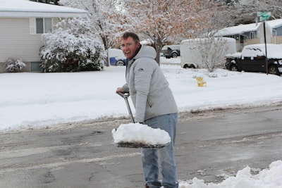 A team member shoveling fresh snow from a residential driveway on a bright winter morning.