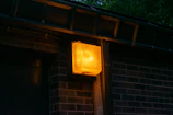 Outdoor Tiverton Power emergency light mounted near a building entrance, shining bright at dusk.