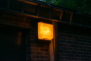 Outdoor Tiverton Power emergency light mounted near a building entrance, shining bright at dusk.