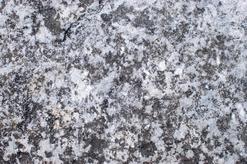 A textured surface featuring a gray, speckled pattern typical of stone or concrete. The irregular shapes and shades of gray create a natural, rugged appearance.