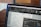 A close-up of a computer screen displaying Adobe InDesign 2023 software. The screen shows a detailed layout of a document with various text, tables, and boxes. The toolbars and text formatting options are visible on the interface. In the background, there's a wooden table and a blurred out-of-focus area.