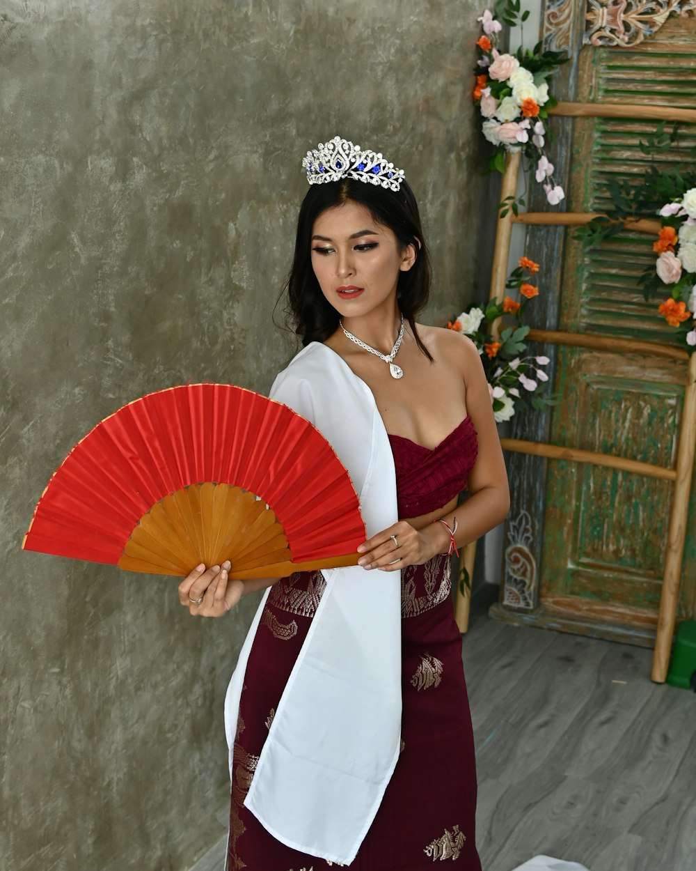 a woman wearing a tiara holding a red fan