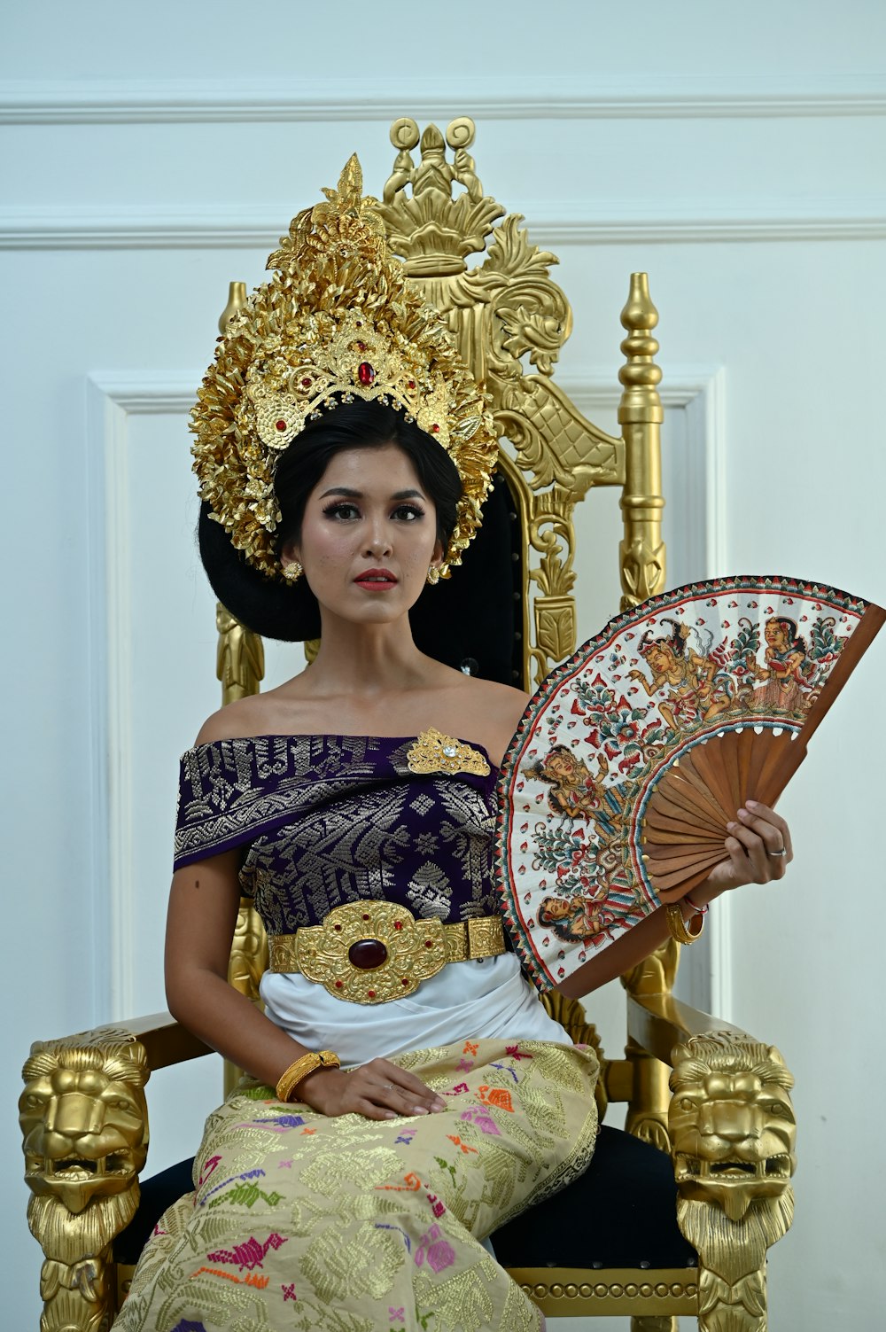 a woman sitting on a golden throne holding a fan