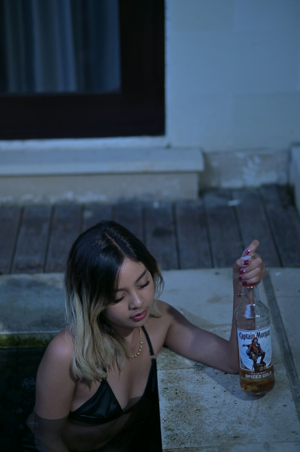 a woman holding a bottle of booze sitting on the ground