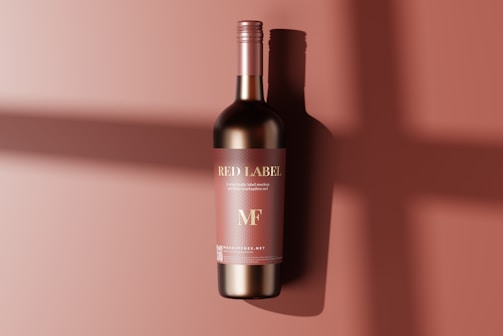 A single wine bottle with a red label against a matching red background. The label features the words 'Red Label' and 'MF' with a subtle shadow of the bottle cast on the surface.