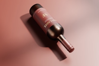 A bottle of red wine lies on its side against a soft, reddish-brown background. The label on the bottle is maroon with gold and white text, creating an elegant appearance. Soft shadows are cast around the bottle, enhancing its three-dimensional look.