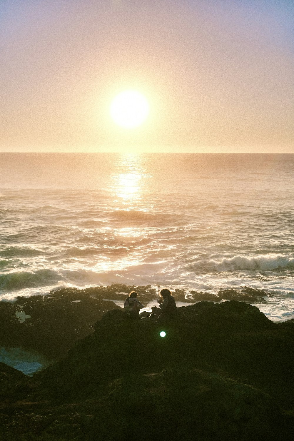 a couple of people sitting on top of a rock near the ocean