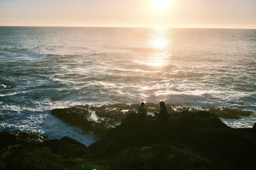 um casal de pessoas sentadas em cima de uma rocha perto do oceano