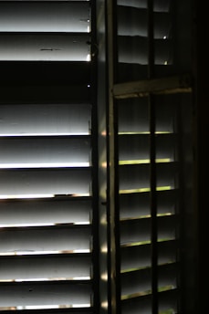 A close-up view of wooden window blinds with light filtering through the slats, casting shadows and highlights.