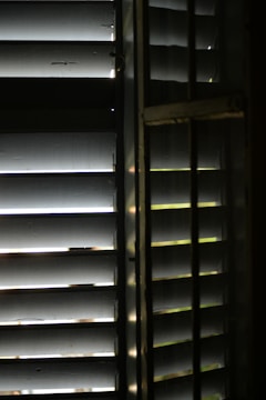 Close-up of sleek wooden blinds partially open, casting warm shadows