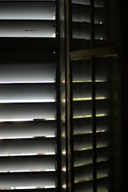 A close-up view of wooden window blinds with light filtering through the slats, casting shadows and highlights.