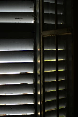 A close-up view of wooden window blinds with light filtering through the slats, casting shadows and highlights.