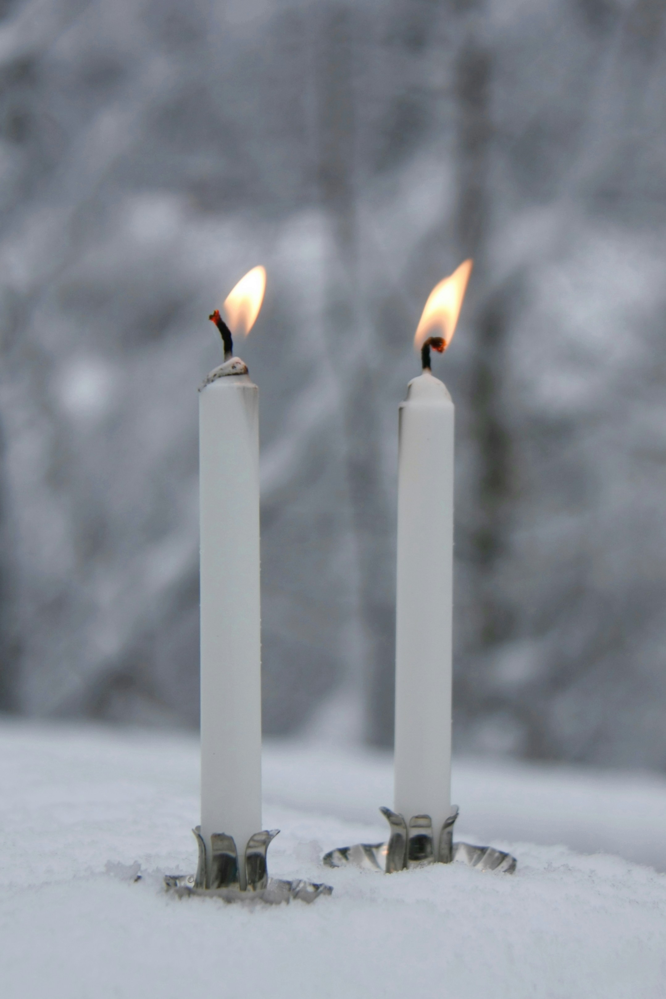 a couple of white candles sitting on top of a snow covered ground
