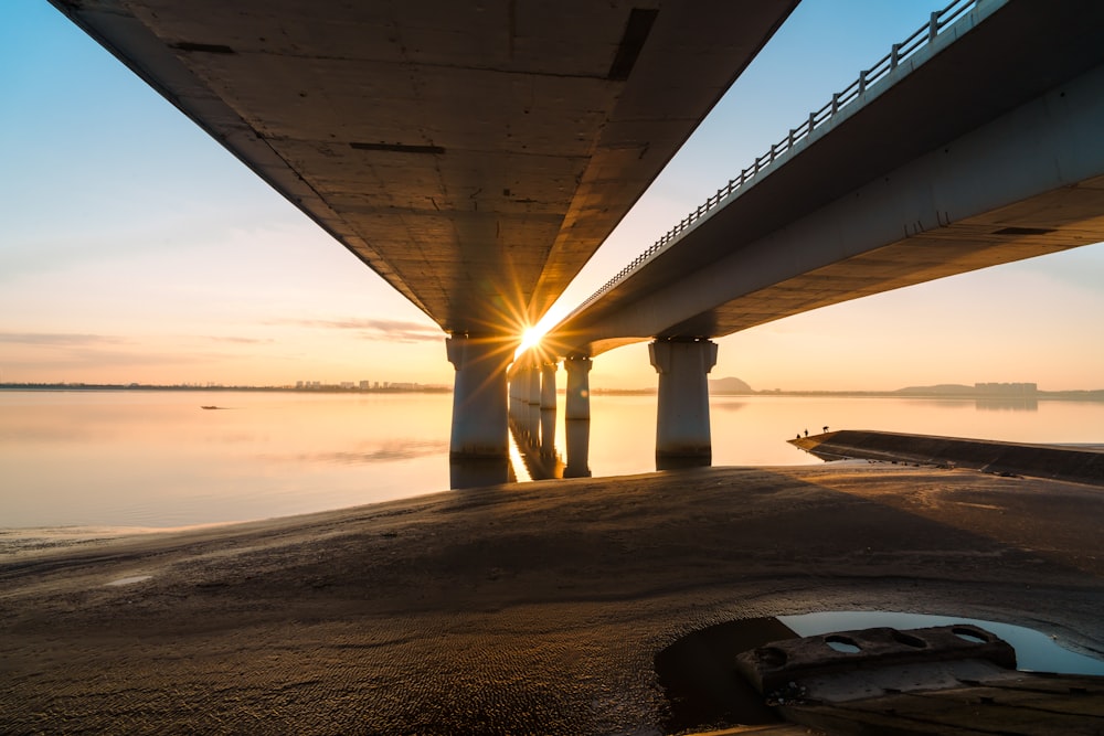the sun is setting under a bridge over a body of water