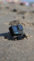 Close-up of a waterproof camera and diving gloves placed on a sandy beach with the sea in the background