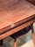 A wooden table with a smooth, polished surface and visible wood grain. It features a brass latch mechanism on the side. There is a wooden chair with a dark seat partially visible underneath the table.
