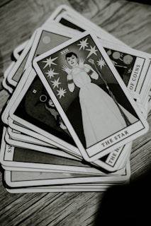 A deck of tarot cards is spread out on a wooden surface. The top card, titled 'The Star,' features an illustration of a person in a stylized white outfit surrounded by stars. The image is in black and white, giving it a vintage appearance.
