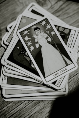 A deck of tarot cards is spread out on a wooden surface. The top card, titled 'The Star,' features an illustration of a person in a stylized white outfit surrounded by stars. The image is in black and white, giving it a vintage appearance.
