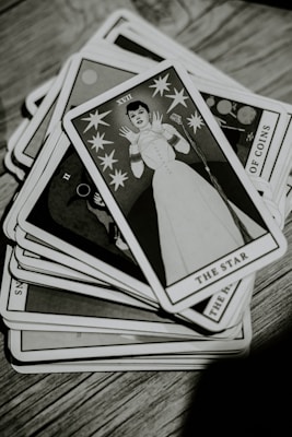 A deck of tarot cards is spread out on a wooden surface. The top card, titled 'The Star,' features an illustration of a person in a stylized white outfit surrounded by stars. The image is in black and white, giving it a vintage appearance.