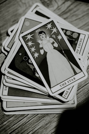 A deck of tarot cards is spread out on a wooden surface. The top card, titled 'The Star,' features an illustration of a person in a stylized white outfit surrounded by stars. The image is in black and white, giving it a vintage appearance.
