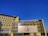 A modern, multi-story building with a contemporary architectural design featuring large windows and a beige facade. A single prominent logo is displayed at the center of the building’s front side. The sky is clear and vividly blue, providing a stark contrast to the building.