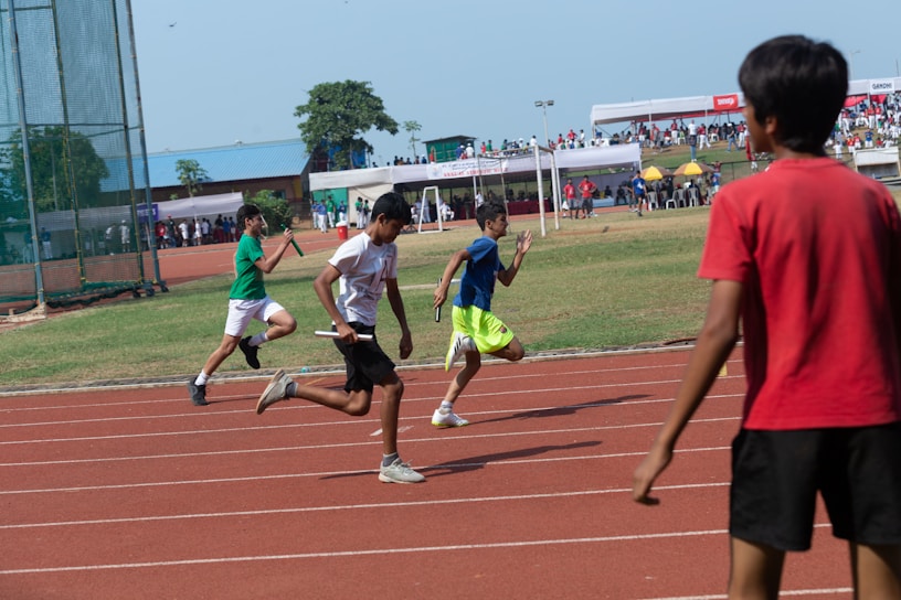 Students in blue and white uniforms sprinting on the school track during a relay race.
