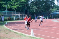 Group of teens practicing relay baton handoffs on a red running track.