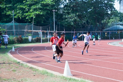Group of teens practicing relay baton handoffs on a red running track.