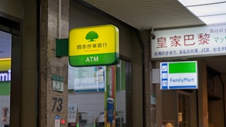 A Cathay United Bank ATM sign is prominently displayed with a yellow and green color scheme. It is located next to a FamilyMart convenience store sign. The setting appears to be indoors with visible elements of a commercial or shopping space, including signage with Chinese and English text.