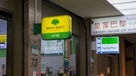 A Cathay United Bank ATM sign is prominently displayed with a yellow and green color scheme. It is located next to a FamilyMart convenience store sign. The setting appears to be indoors with visible elements of a commercial or shopping space, including signage with Chinese and English text.