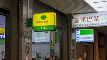 A Cathay United Bank ATM sign is prominently displayed with a yellow and green color scheme. It is located next to a FamilyMart convenience store sign. The setting appears to be indoors with visible elements of a commercial or shopping space, including signage with Chinese and English text.