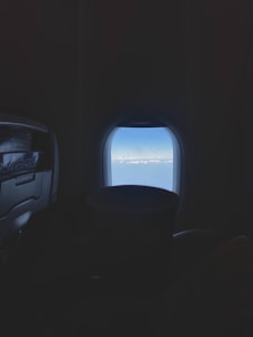 Comfortable airplane seats with a window view of blue sky and clouds.