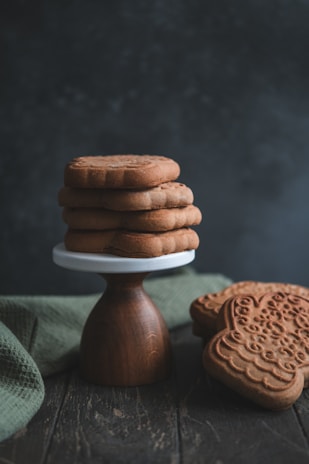 Close-up of a stack of chocolate-dipped lotus cookies on a rustic wooden table with soft natural light.