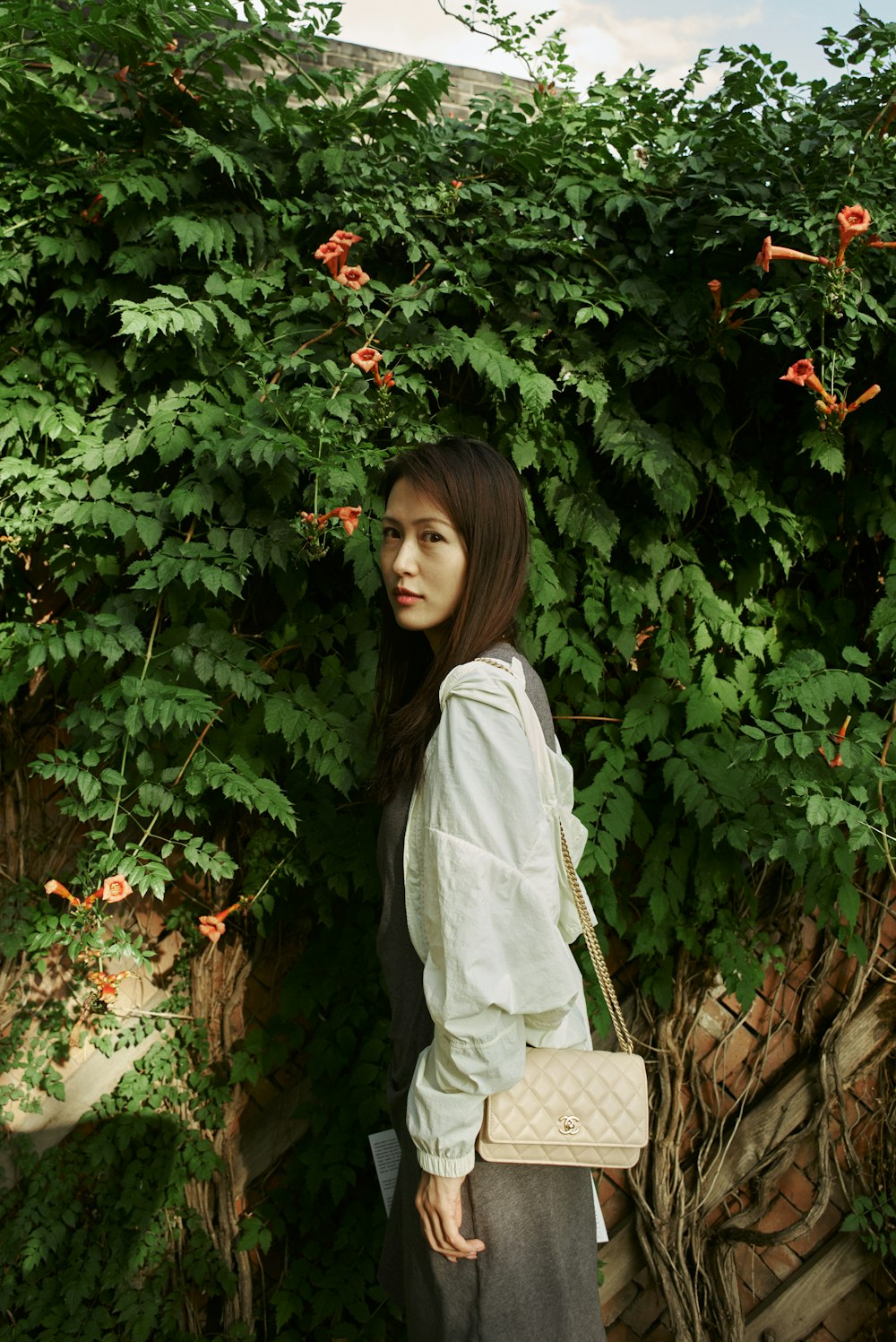 a woman standing in front of a bush holding a purse