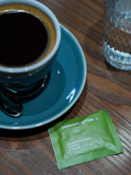 A steaming cup of soluble coffee next to a small packet on a wooden table.