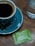 Close-up of a steaming cup of black coffee next to a small instant coffee packet on a wooden table.
