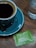 Close-up of a steaming cup of black coffee next to a small instant coffee packet on a wooden table.