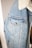 A close-up view of a light blue denim jacket featuring prominent stitching details, metal button closures, and a white faux fur collar. The texture of the denim fabric is clearly visible, providing a casual and comfortable appearance.