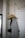 A coat hanger on a wall holds a grey coat and a wide-brimmed tan hat. Above, a string of lights with visible cords drapes along the wall. A partially visible door is on the right, featuring a modern handle. The setting appears to be indoors, possibly an entryway or hallway.
