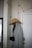A coat hanger on a wall holds a grey coat and a wide-brimmed tan hat. Above, a string of lights with visible cords drapes along the wall. A partially visible door is on the right, featuring a modern handle. The setting appears to be indoors, possibly an entryway or hallway.